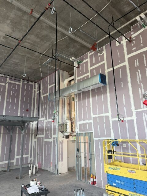 Sheet metal duct and overhead piping being run in a high-bay commercial space